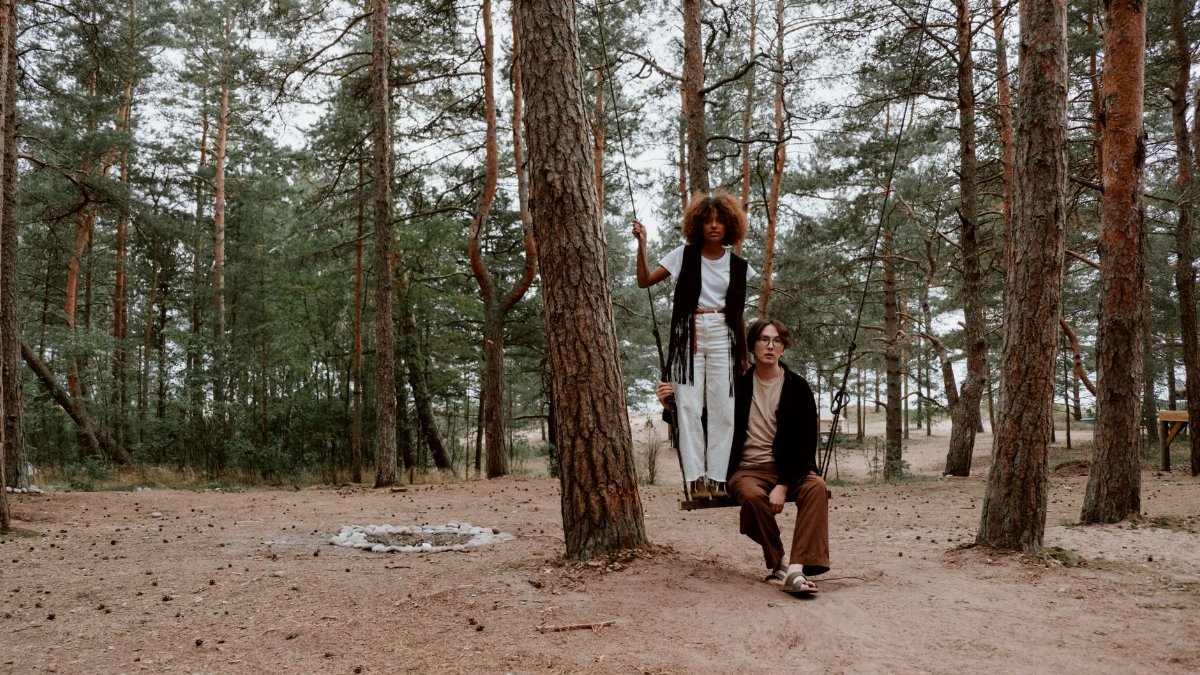 A couple sitting on a swing in a serene forest campsite setting.