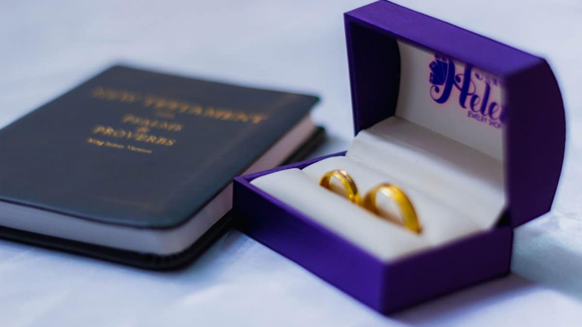 Beautiful gold wedding rings in a purple box beside a New Testament Bible, representing marriage and faith.