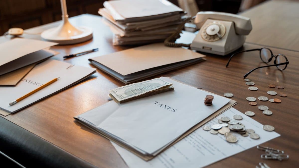 Close-up of an office desk with tax documents, coins, glasses, and an old phone, symbolizing finance and organization.