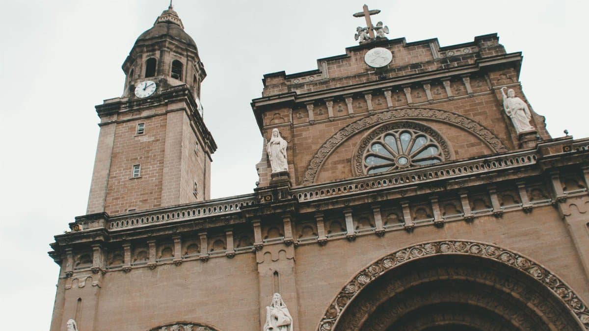A dramatic view of the Manila Cathedral showcasing its neo-romanesque architecture with statues and clock tower.