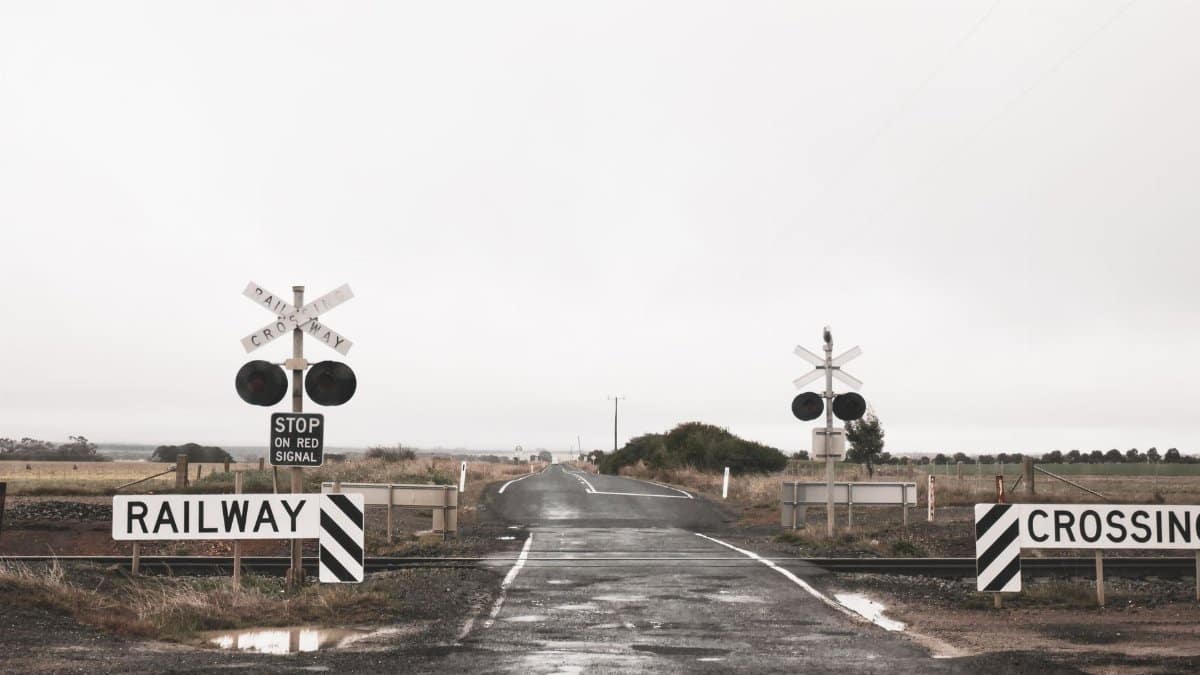 Quiet railway crossing in rural Australia with cloudy skies and wet road conditions.
