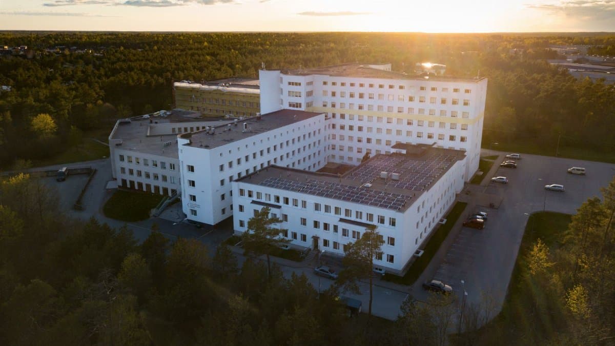 Aerial view of a modern hospital building surrounded by greenery at sunset, illustrating serene healthcare environment.
