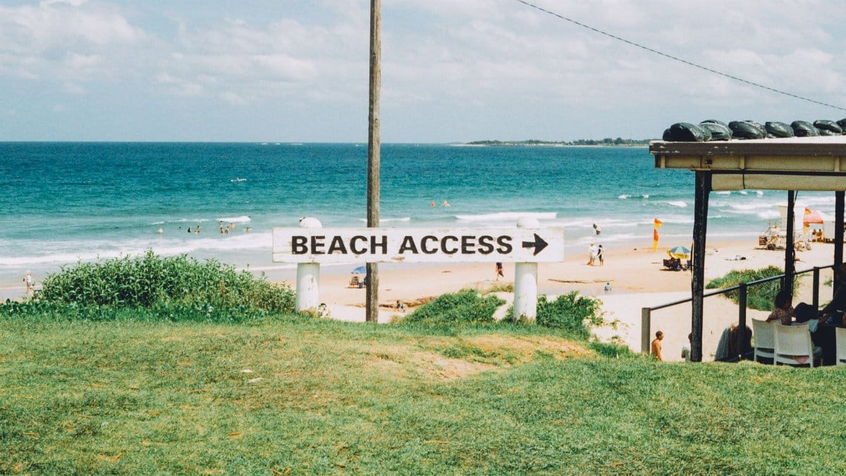 A scenic view of a beach access sign pointing towards the sandy shores at Wollongong, NSW, Australia.