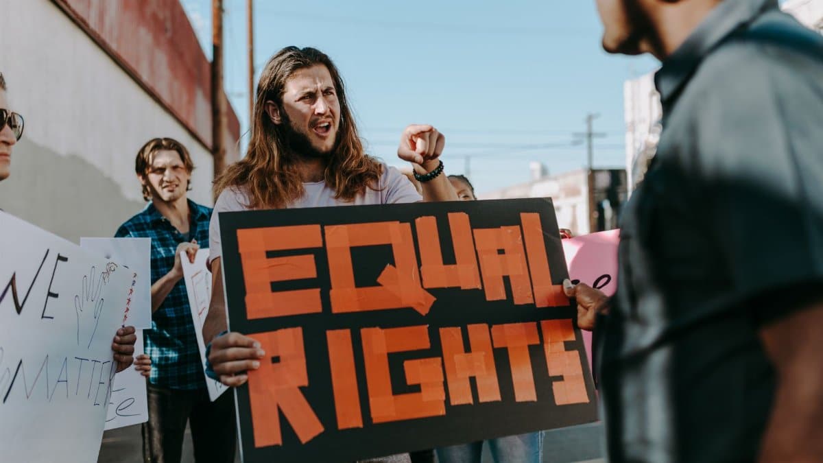 Protesters holding signs advocating equal rights during a rally on a sunny day.
