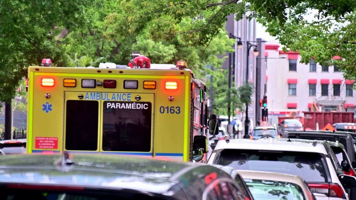 Ambulance caught in urban traffic amidst green trees, focused on emergency response.