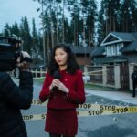 Journalist reporting live from a taped crime scene with cameraman and police.
