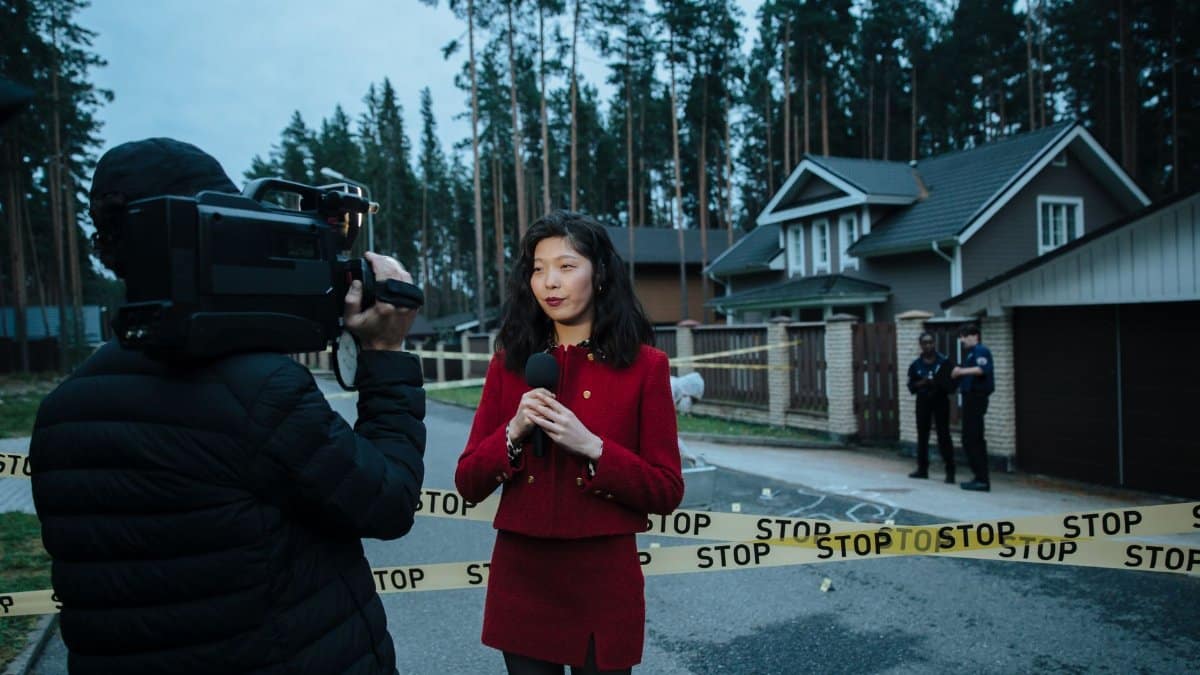 Journalist reporting live from a taped crime scene with cameraman and police.