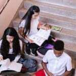 A group of teenagers studying and reading books while sitting on a staircase indoors.