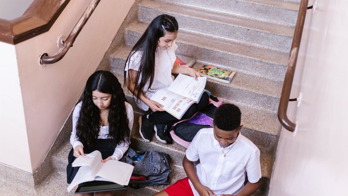 A group of teenagers studying and reading books while sitting on a staircase indoors.