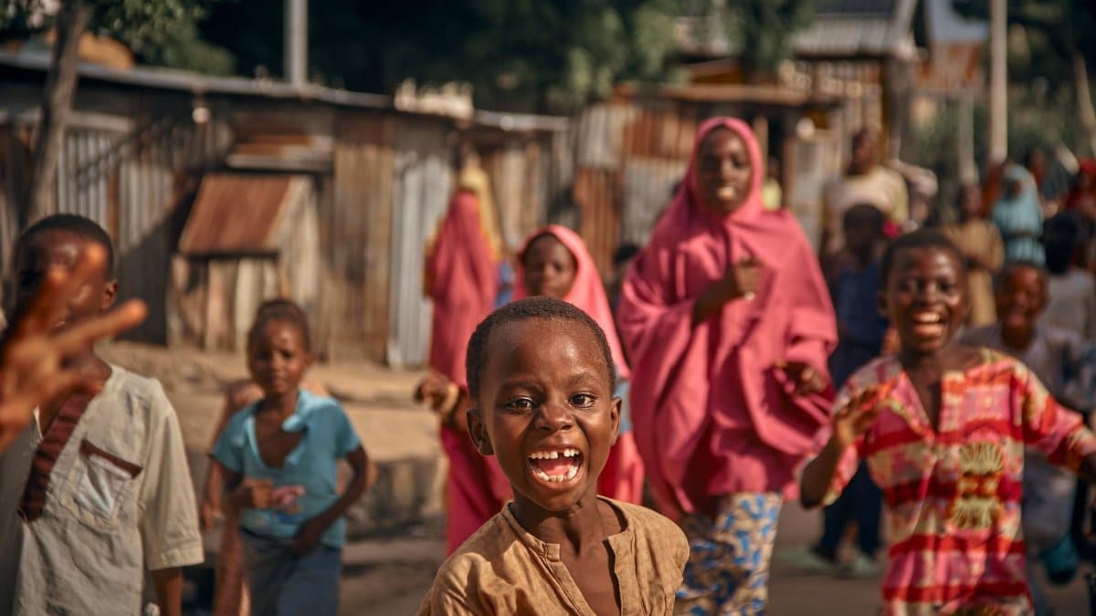 Children laughing and playing in a vibrant African village street scene, full of energy.