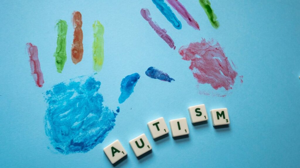 Colorful child handprints and autism text on a blue background, promoting awareness.