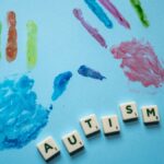 Colorful child handprints and autism text on a blue background, promoting awareness.