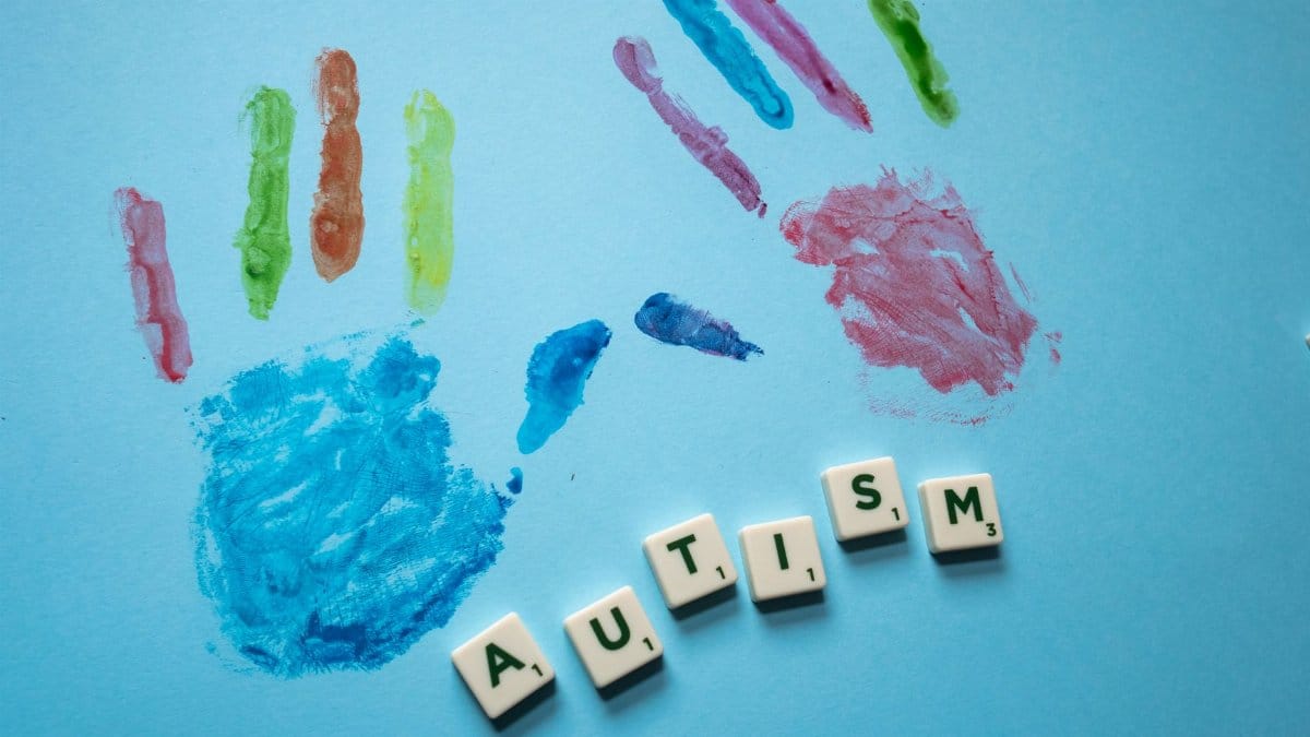 Colorful child handprints and autism text on a blue background, promoting awareness.