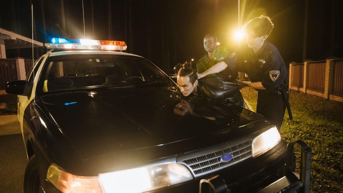 Police officers apprehending a suspect at night under streetlights by a patrol car.