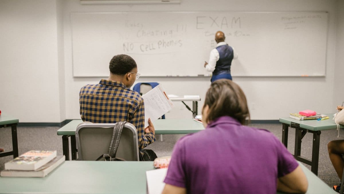 Students in a college classroom taking an exam with rules written on the board.