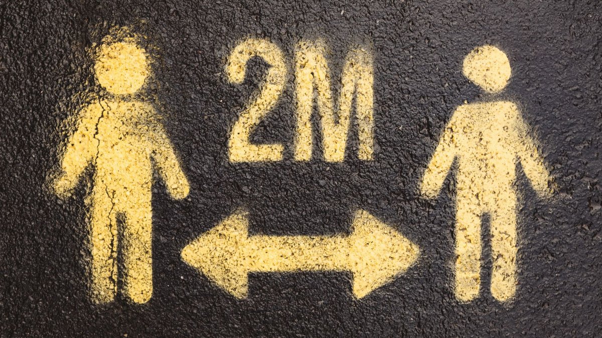 A yellow spray-painted sign on asphalt indicating social distancing with figures and an arrow.