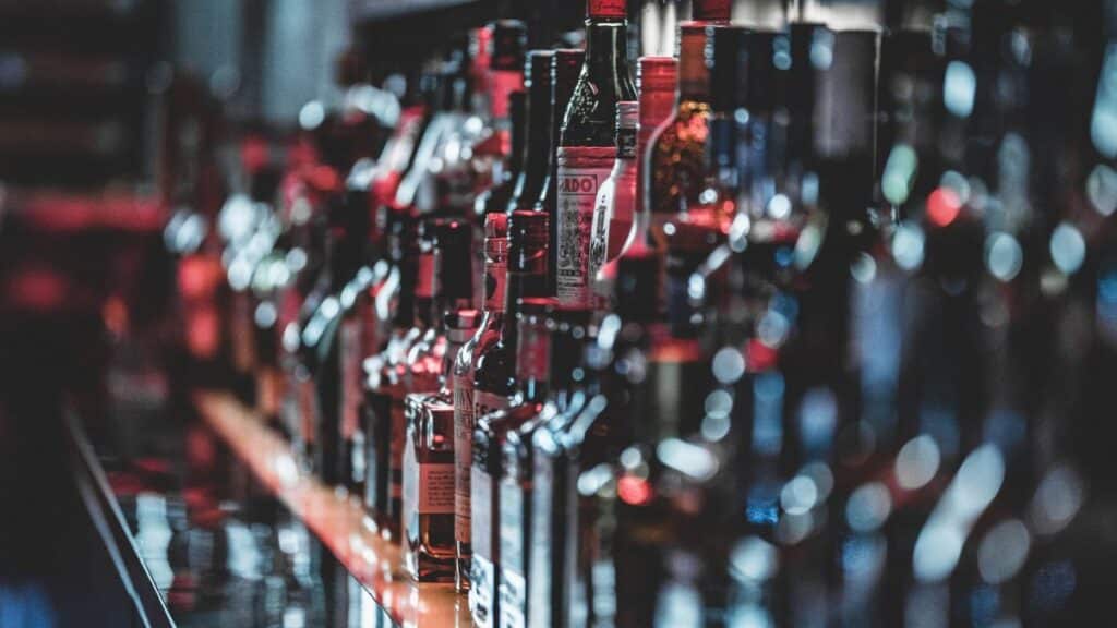 Blurred view of assorted alcohol bottles lined up on a bar shelf indoors.