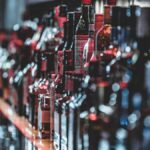 Blurred view of assorted alcohol bottles lined up on a bar shelf indoors.