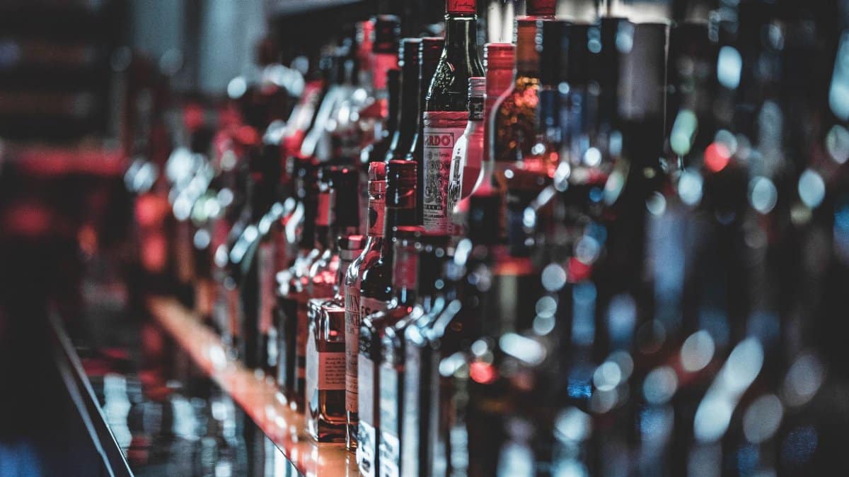 Blurred view of assorted alcohol bottles lined up on a bar shelf indoors.