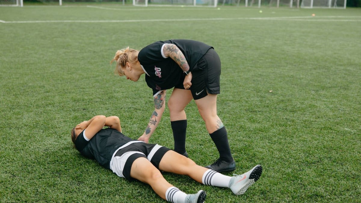 A female soccer player helps an injured teammate on a green soccer field during a game.
