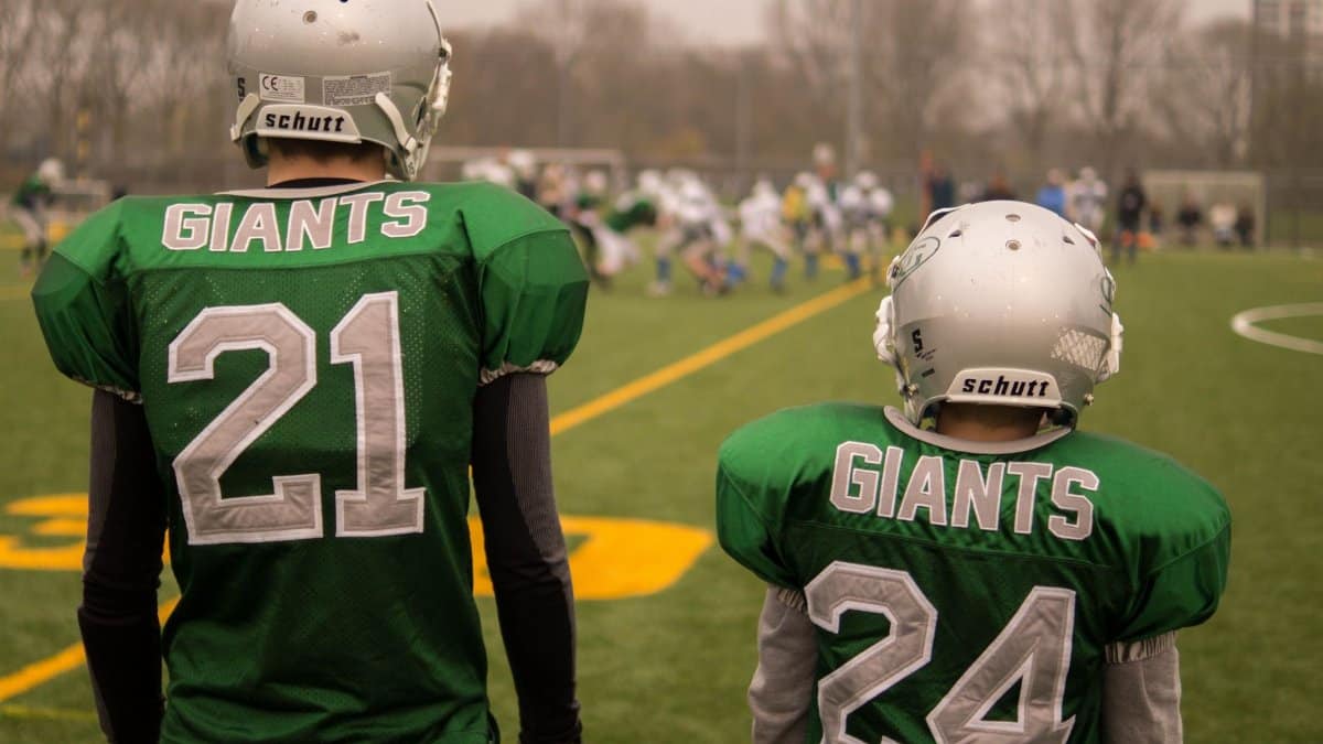 Two football players, wearing green Giants jerseys, preparing for a match on a field.