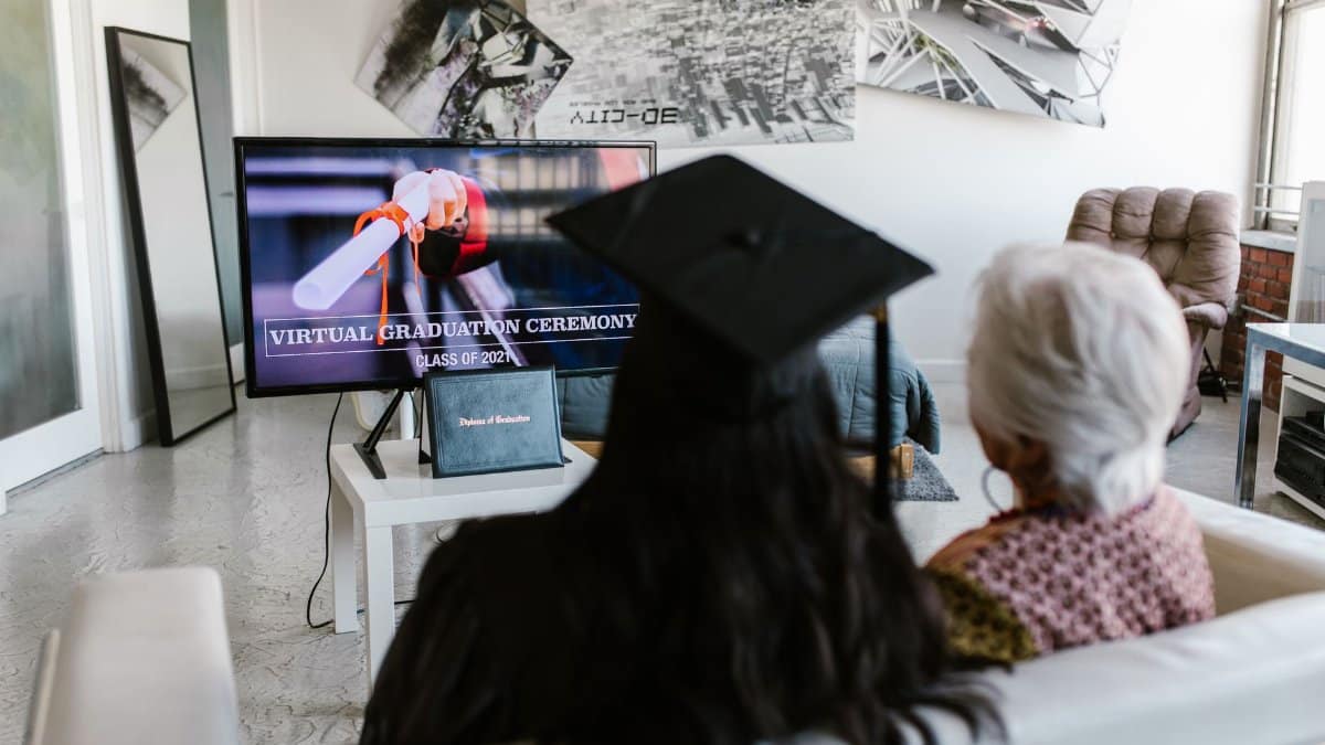 Two people watching a virtual graduation ceremony together at home, capturing the new normal of online celebrations.