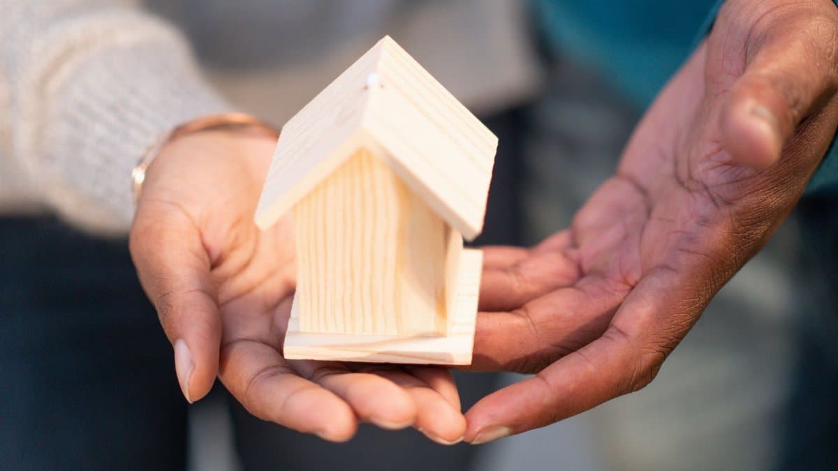 Close-up of hands holding a small wooden house, representing real estate and new home ownership.