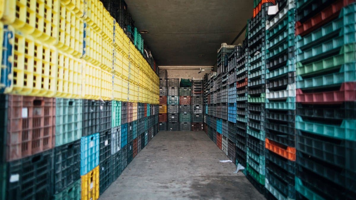 Empty passage with cement floor between heaps of colorful plastic boxes and pallets in rows in warehouse