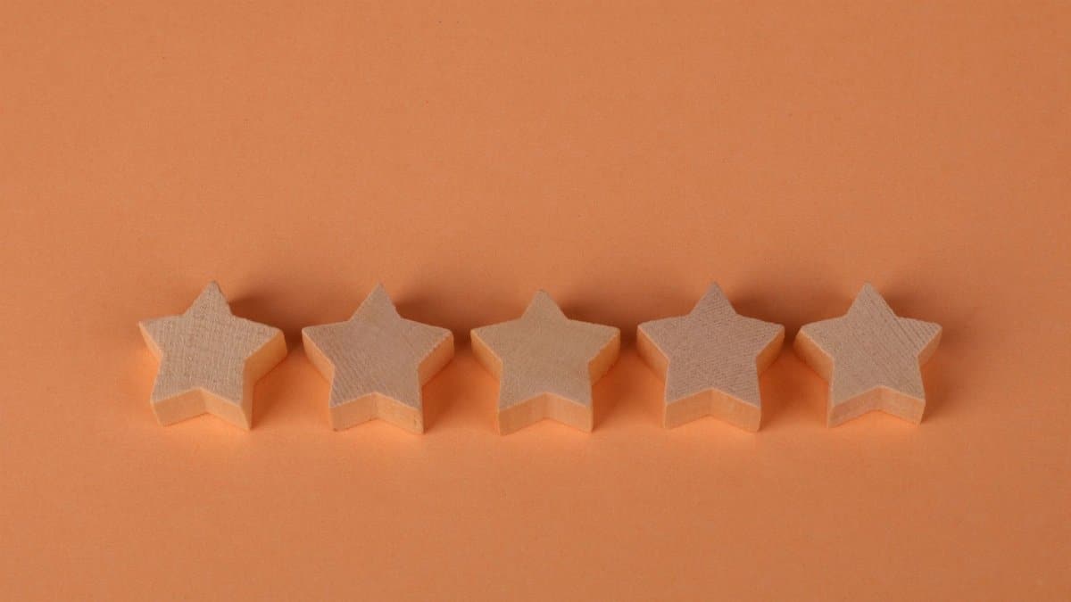 Five wooden star-shaped blocks arranged on an orange surface, perfect for rating concepts.