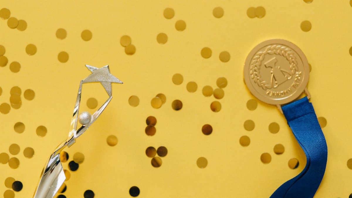 Golden medal and silver trophy with confetti on yellow surface, celebrating achievement.