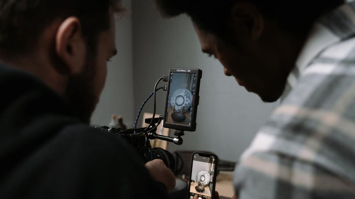 Two men use cameras and smartphones to capture a close-up video in a studio setting.