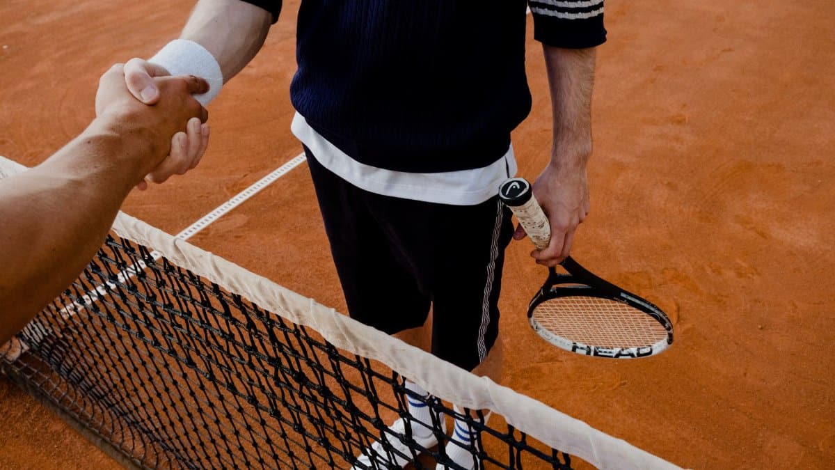 A close-up of tennis players shaking hands over the net on a clay court.