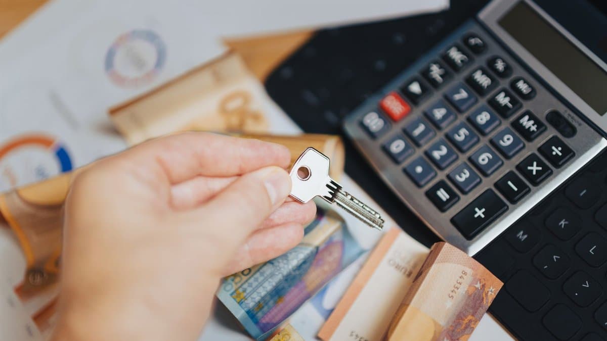 Hand holding key above Euro banknotes and calculator, symbolizing real estate investment.