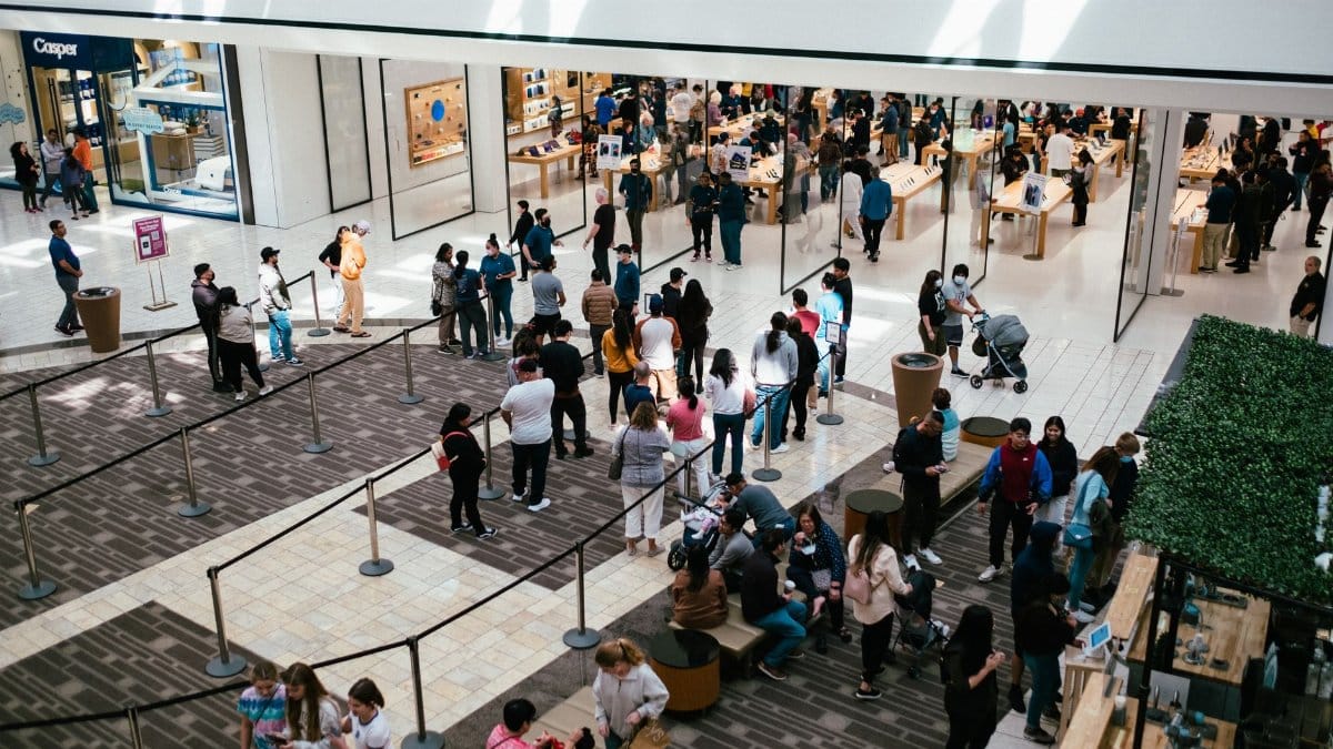 A bustling shopping center with a large crowd queuing inside an Apple Store.