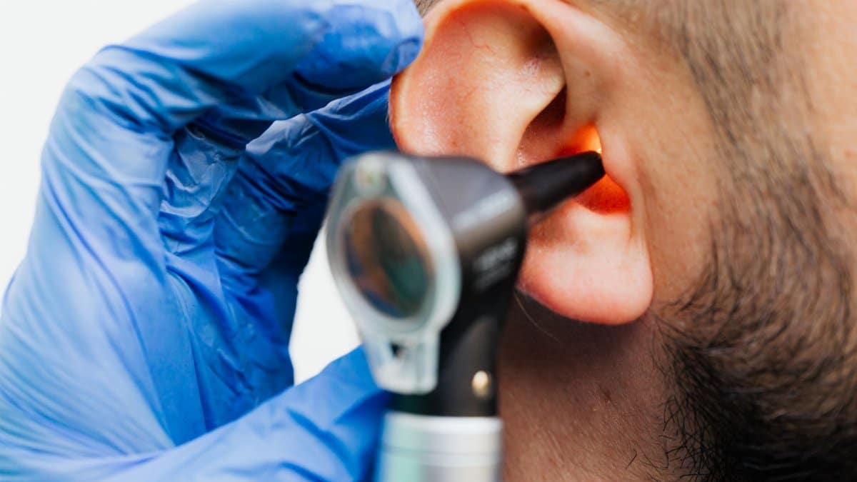 Close-up of a doctor using an otoscope to examine a patient's ear in a clinical setting.