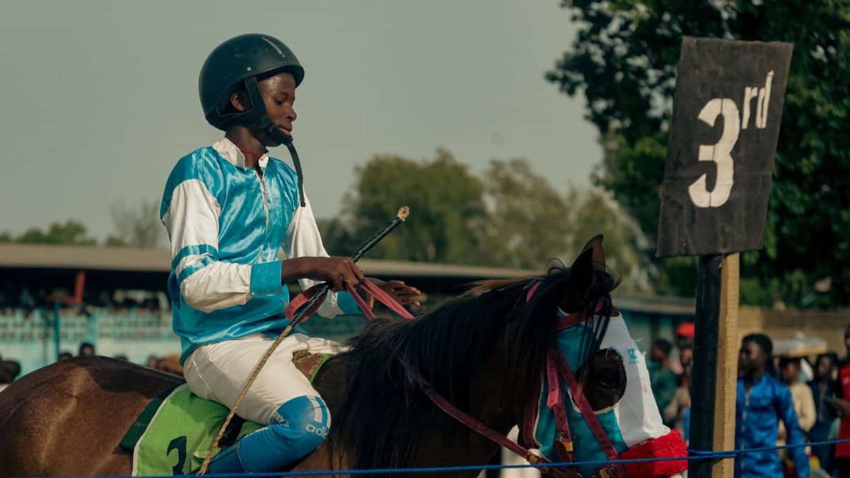 A young equestrian competing in a horse race, finishing in third place, under a clear sky.