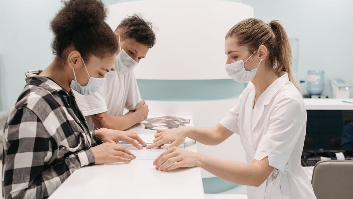 A healthcare professional in a medical setting assists patients at a clinic desk, emphasizing care and teamwork.