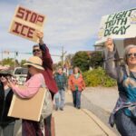 A diverse group peacefully protests in Towson, Maryland, holding signs for various causes.