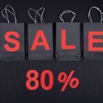 Highlighting a sale with 80% discount using black shopping bags and bold red text.