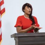 A confident woman delivers a speech at a podium with the US flag, symbolizing leadership and diplomacy.