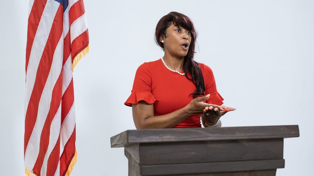 A confident woman delivers a speech at a podium with the US flag, symbolizing leadership and diplomacy.