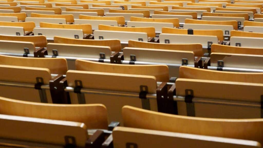 Image of empty wooden seats in an academic auditorium, located indoors.