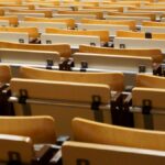 Image of empty wooden seats in an academic auditorium, located indoors.