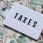 From above of white retro lightbox with TAXES inscription placed on pile of USA dollar bills on white surface
