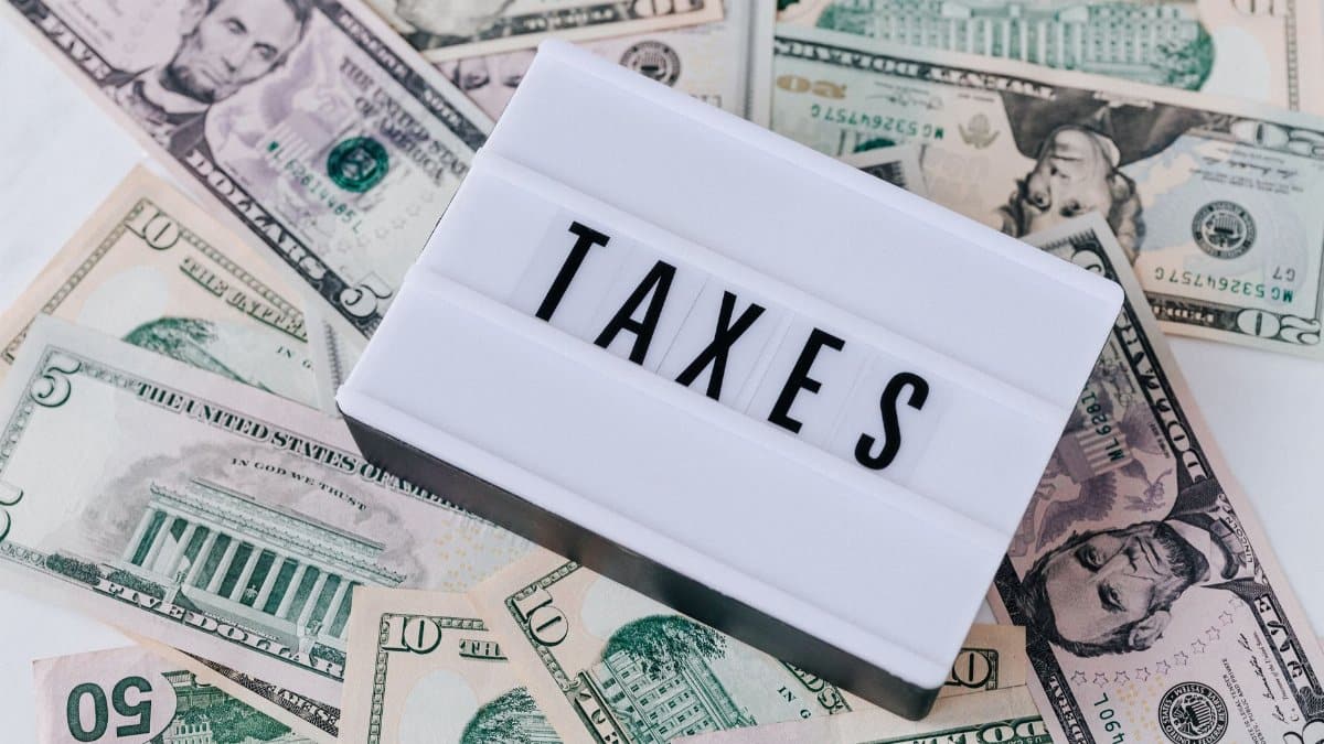 From above of white retro lightbox with TAXES inscription placed on pile of USA dollar bills on white surface