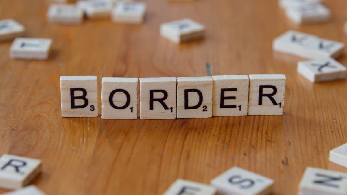 Close-up of scrabble tiles spelling 'border' against a wooden background, symbolizing boundaries.