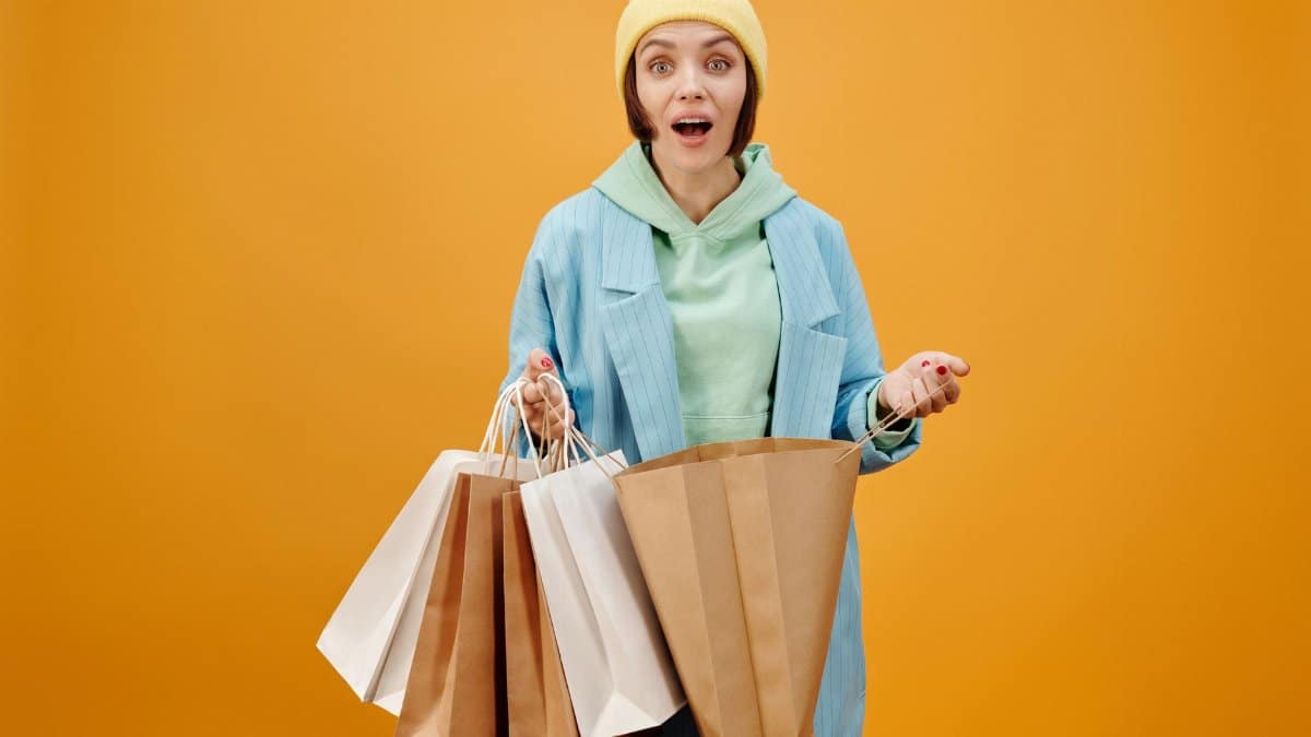 A woman in vibrant clothes holds several shopping bags against a solid background.