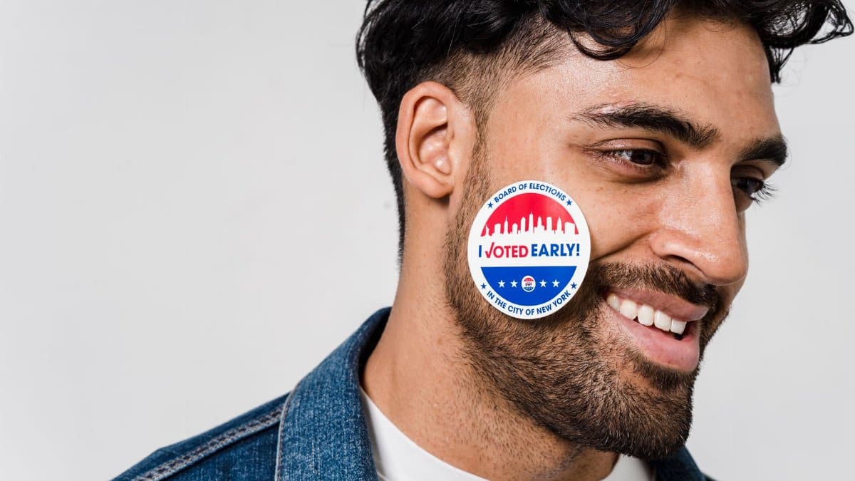 Smiling young man with 'I Voted Early' sticker on cheek, demonstrating civic participation.