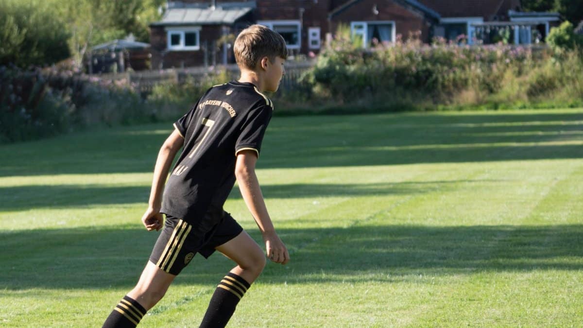 A teenager in sportswear playing soccer on a sunny day near a rural home.