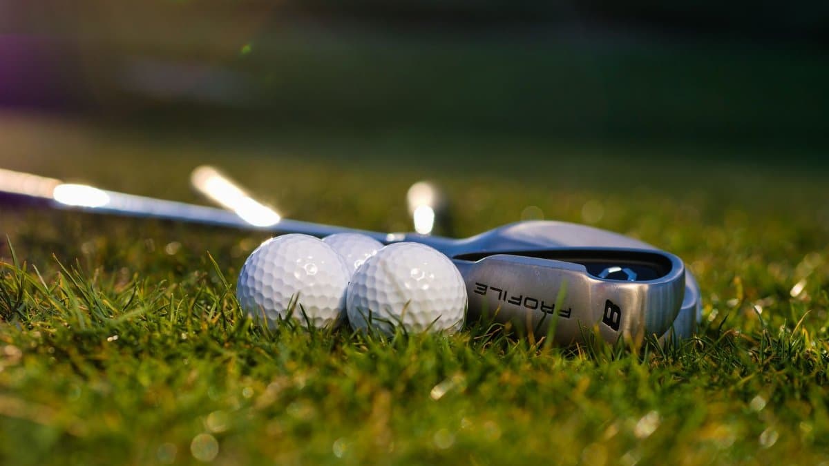 Golf balls and club on a lush green field with warm natural lighting.